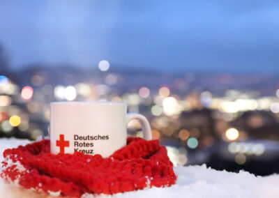 DRK-Tasse mit heißem Tee, eingehüllt in Strickschal vor Stuttgarter Winterlandschaft